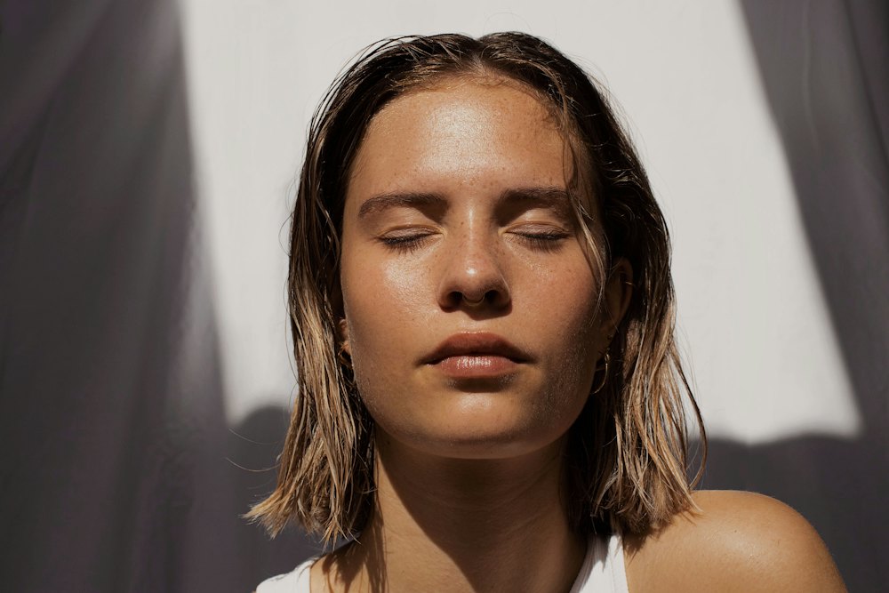 Woman with eyes closed and dewy skin in a shaft of light