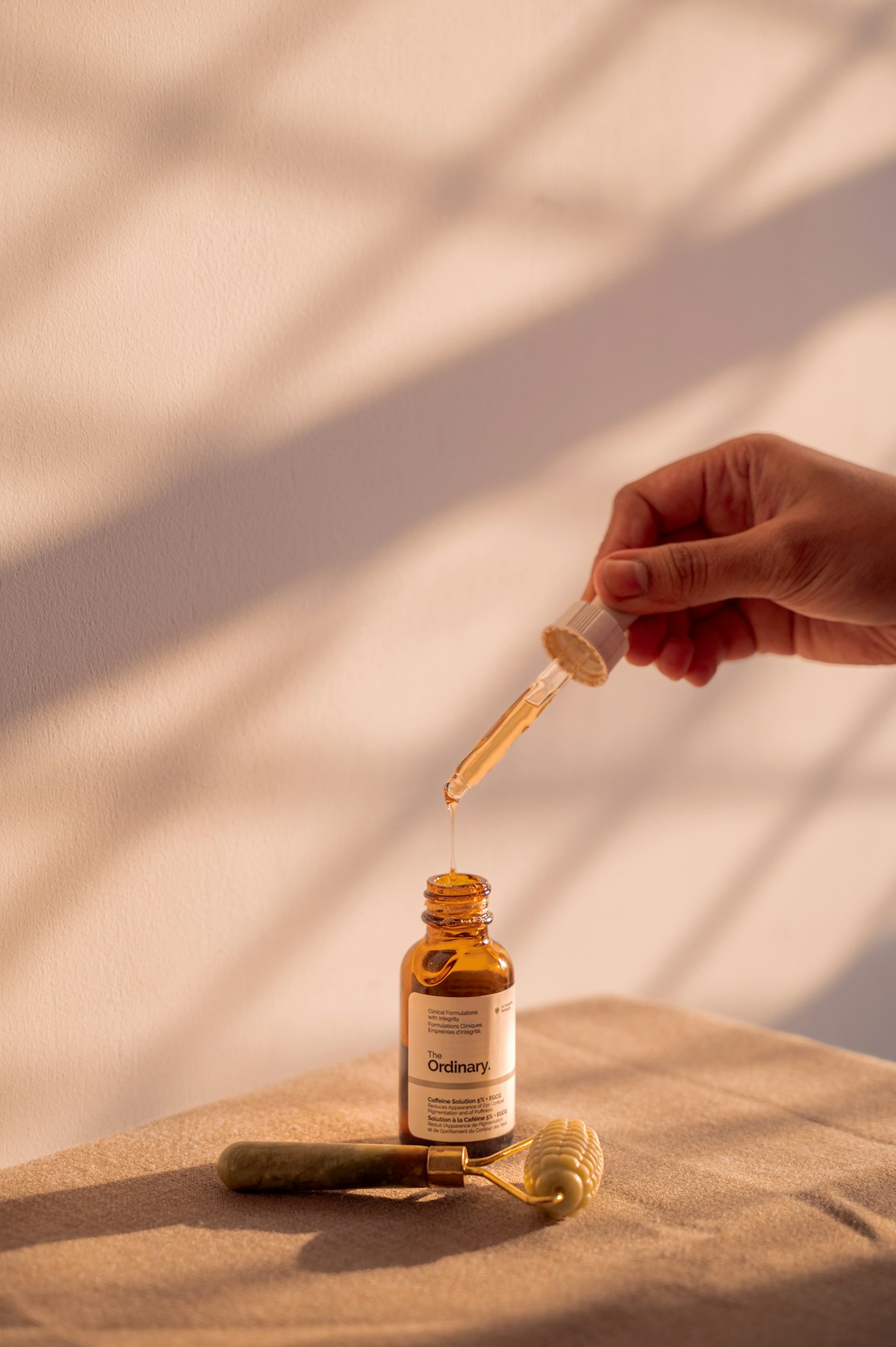 Hand holding a dropper bottle over a serum bottle in warm light